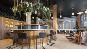 A bar area with wooden bar stools, hanging plants, and pendant lighting. - Boutique Suite | Rooftop | Convention Ctr (New Orleans)