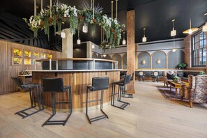 Eine Bar mit Holzhockern, hängenden Pflanzen und Pendelleuchten.