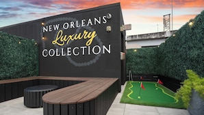 A wall with 'NEW ORLEANS Luxury Collection' signage, a wooden bench, and a miniature golf setup. - Boutique Suite | Rooftop | Convention Ctr (New Orleans)