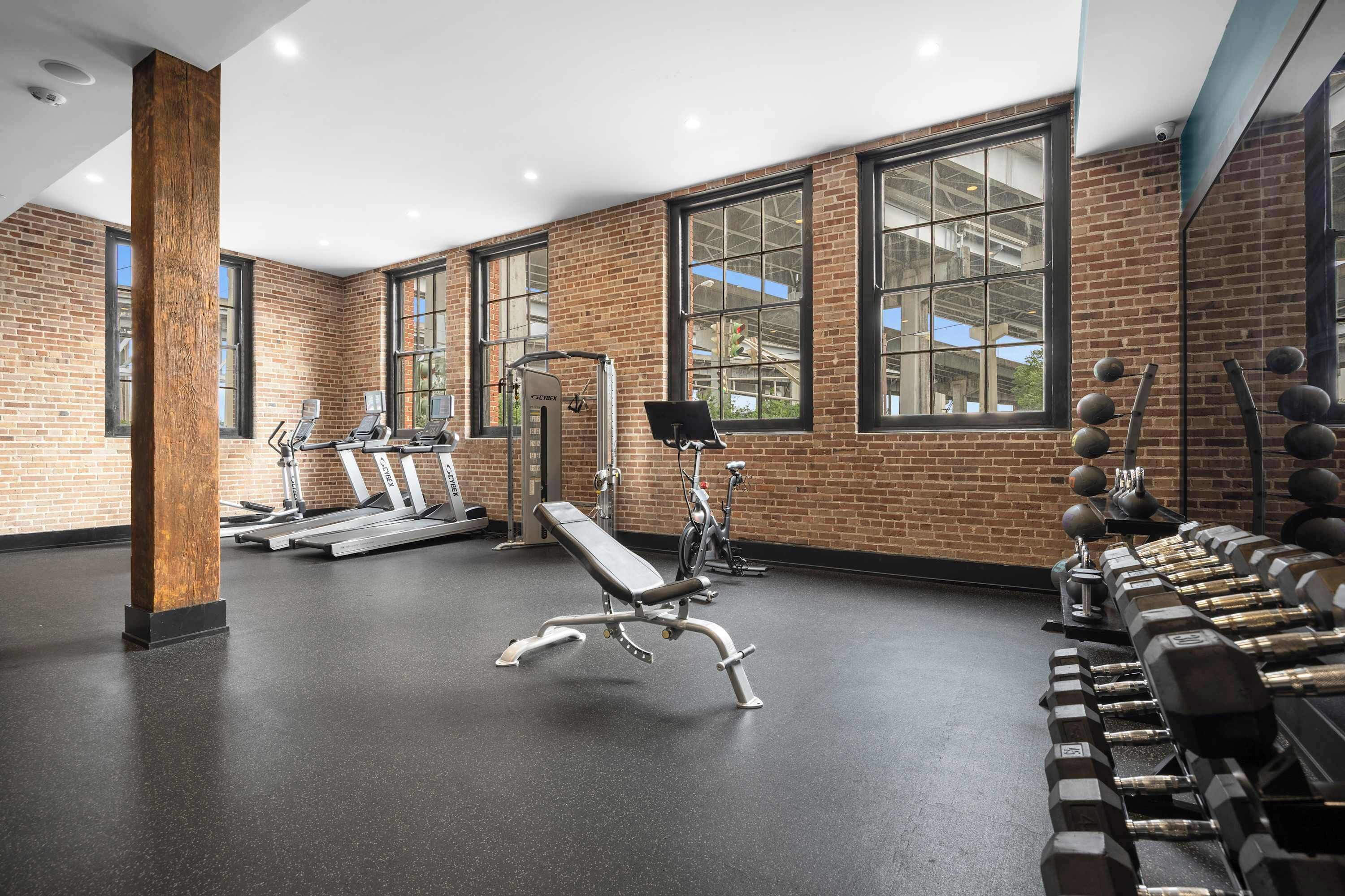 A gym with brick walls, large windows, and various exercise equipment.