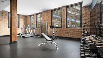 A gym with brick walls, large windows, and various exercise equipment.