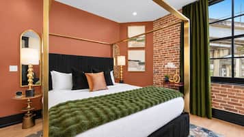A hotel room with a four-poster bed, a brick accent wall, a large window with curtains, and a green throw blanket.