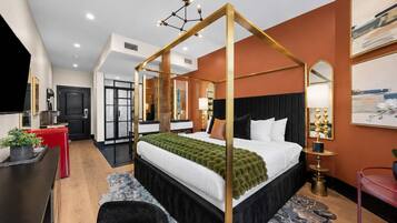 A modern hotel room with a four-poster bed, a desk with a chair, a small table, and a red cabinet.