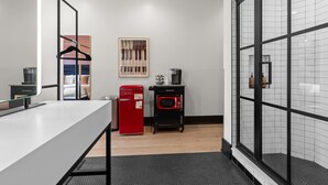 A modern hotel room with a kitchenette, a large mirror, a bed with a headboard, and a view through a glass door. - Boutique Suite | Rooftop | Convention Ctr (New Orleans)