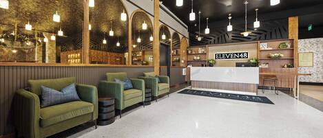 A hotel lobby with green sofas, a reception desk, and a sign reading 'ELEVEN48'.