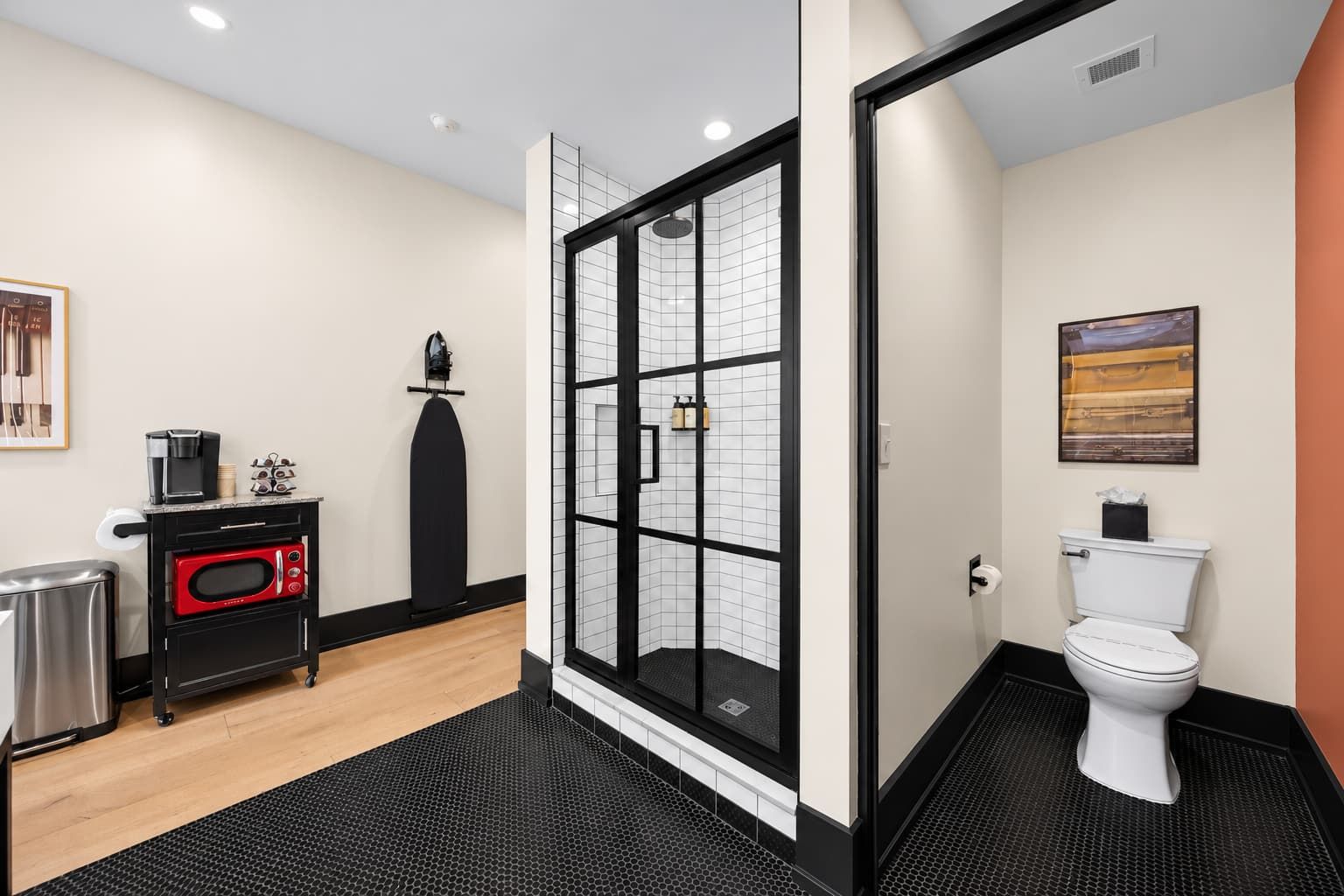 A modern bathroom with a glass shower enclosure, a toilet, and a compact kitchenette with a coffee maker.