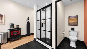 A modern bathroom with a glass shower enclosure, a toilet, and a compact kitchenette with a coffee maker.
