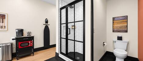 A modern bathroom with a glass shower enclosure, a toilet, and a compact kitchenette with a coffee maker.