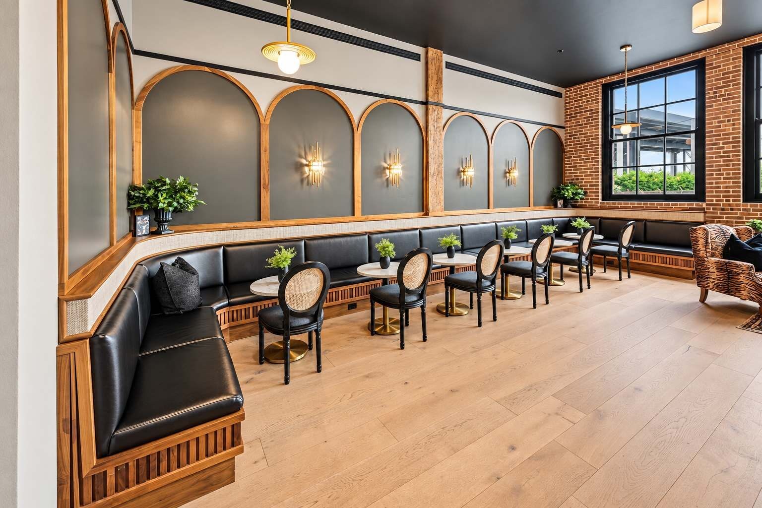 A restaurant with a long counter, black leather seating, and a brick wall.