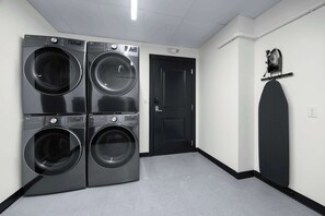 A laundry room with four stacked front-loading washing machines, a black door, and a wall-mounted drying rack. - Sleeps 10 | Luxury 4BR Downtown (New Orleans)
