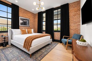 A modern bedroom with a large bed, a desk, and a chair, featuring brick walls and large windows. - Sleeps 10 | Luxury 4BR Downtown Hotel (New Orleans)