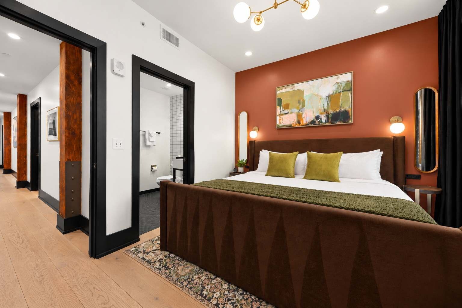 Une chambre d’hôtel avec un grand lit, un tableau au mur et une vue sur le couloir.