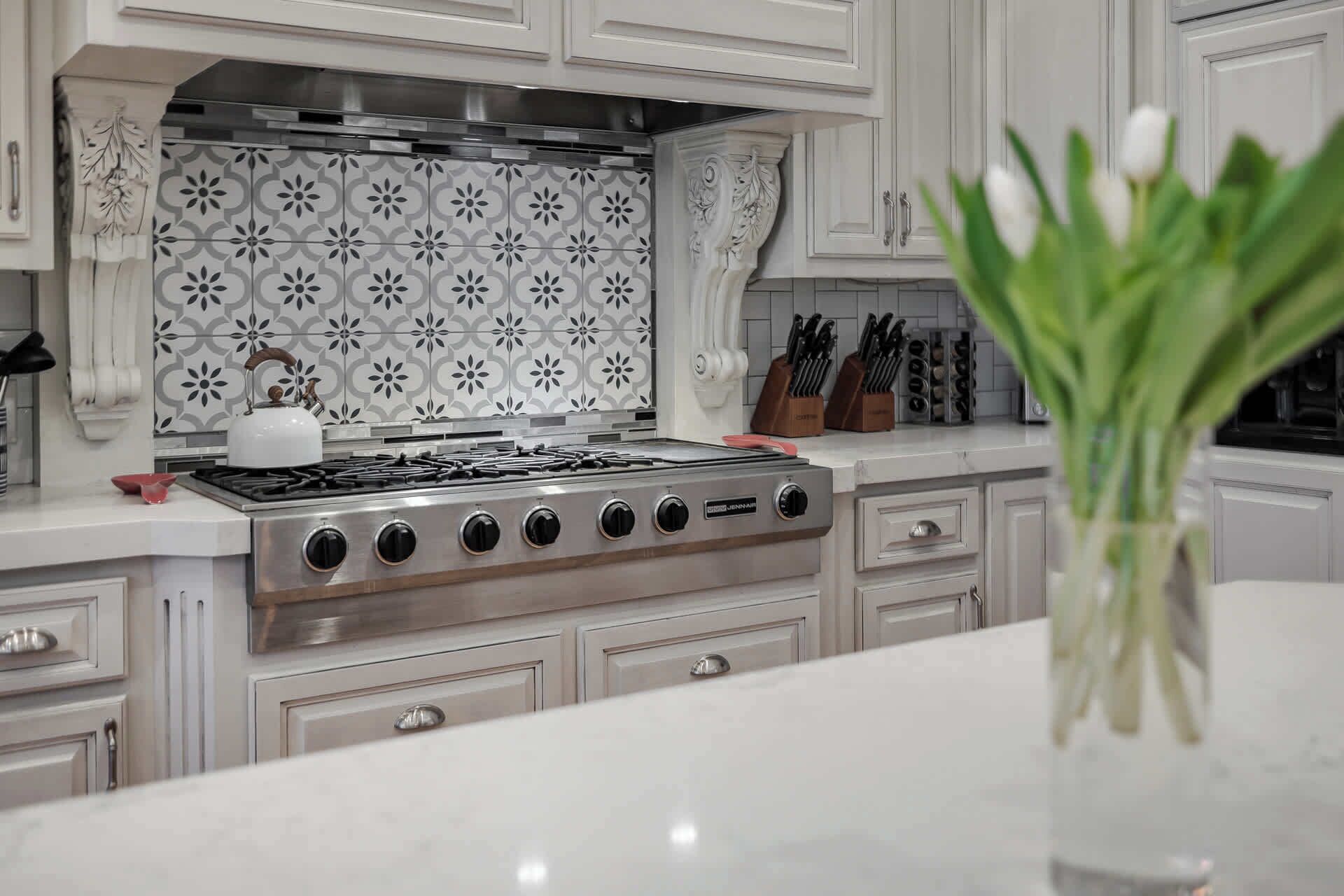 Une cuisine équipée d’une cuisinière à gaz, de meubles blancs et d’un crédence décorée.