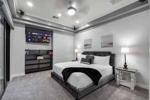 A modern hotel room with a bed, two bedside tables, a wall-mounted TV, and a bookshelf. - The Estate | Lake Views w/Heated Pool, Spa, & Dock (Glendale)