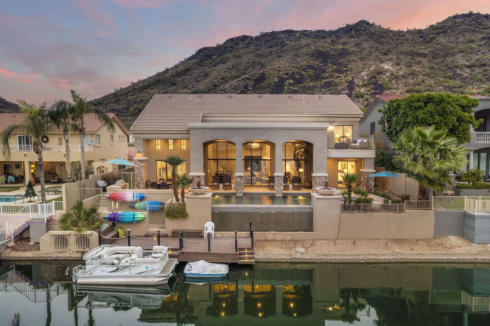 A large house with a pool, docked boats, and a mountain in the background.