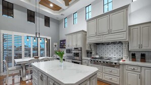 A spacious kitchen with white cabinetry, a large island, and a dining area with a table and chairs. - The Estate | Lake Views w/Heated Pool, Spa, & Boat (Glendale)