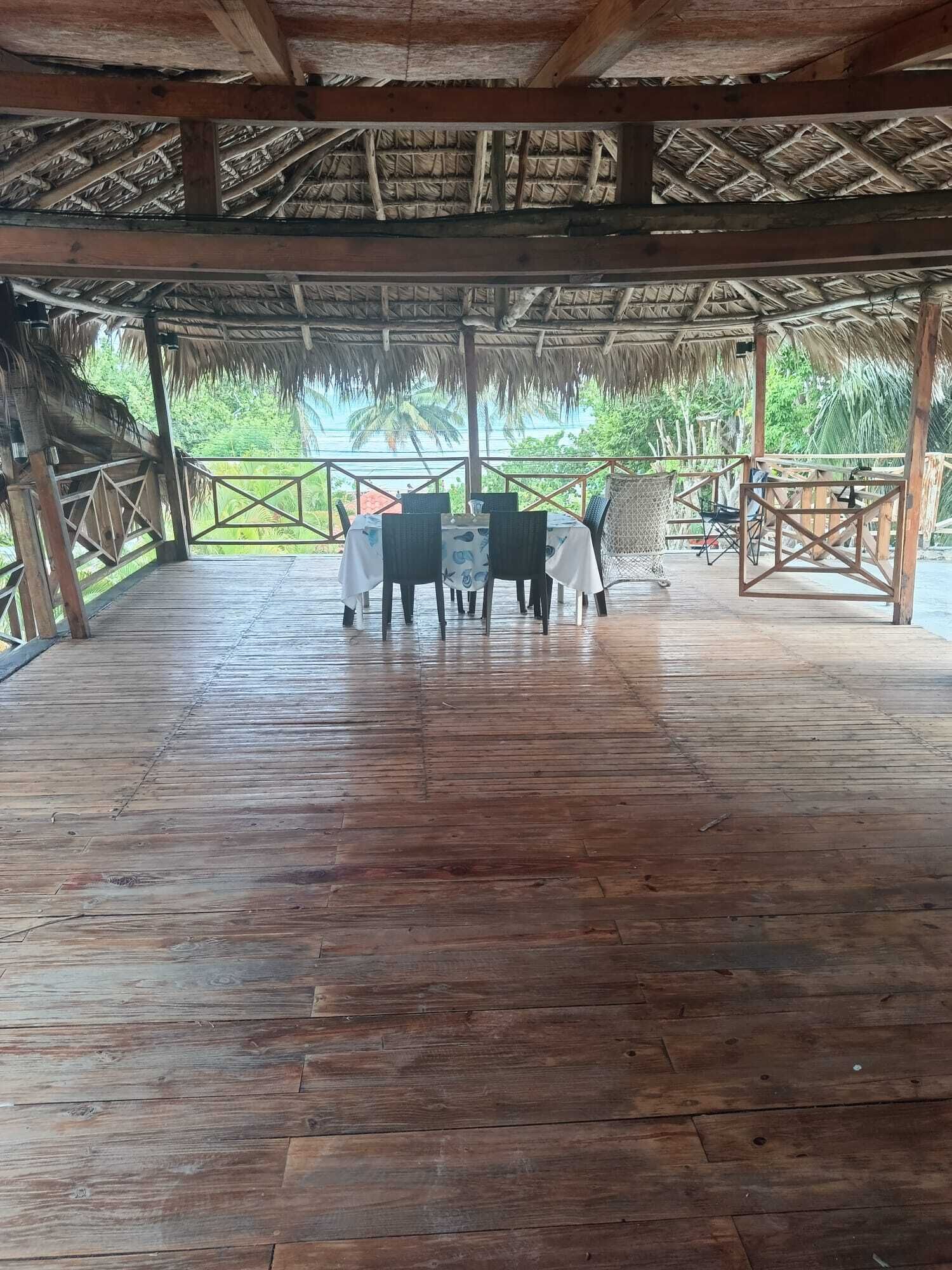 Una terrazza in legno scoperta con tetto di paglia, circondata da una ringhiera in metallo, con vista su un paesaggio tropicale.