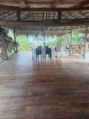 Una terrazza in legno scoperta con tetto di paglia, circondata da una ringhiera in metallo, con vista su un paesaggio tropicale.
