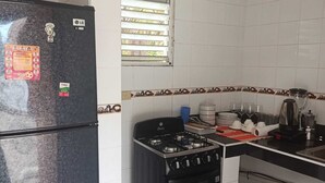 Cocina compacta con refrigerador, estufa, horno y una ventana con persianas.