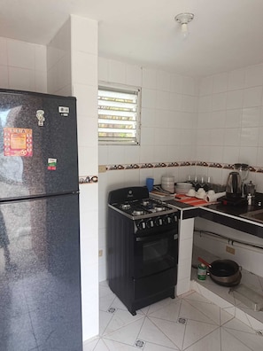 Una cucina compatta con frigorifero, fornello, forno e una finestra con persiane.