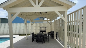 Ein überdachter Patio-Bereich mit Pool, Gartenmöbeln und einer Umzäunung.