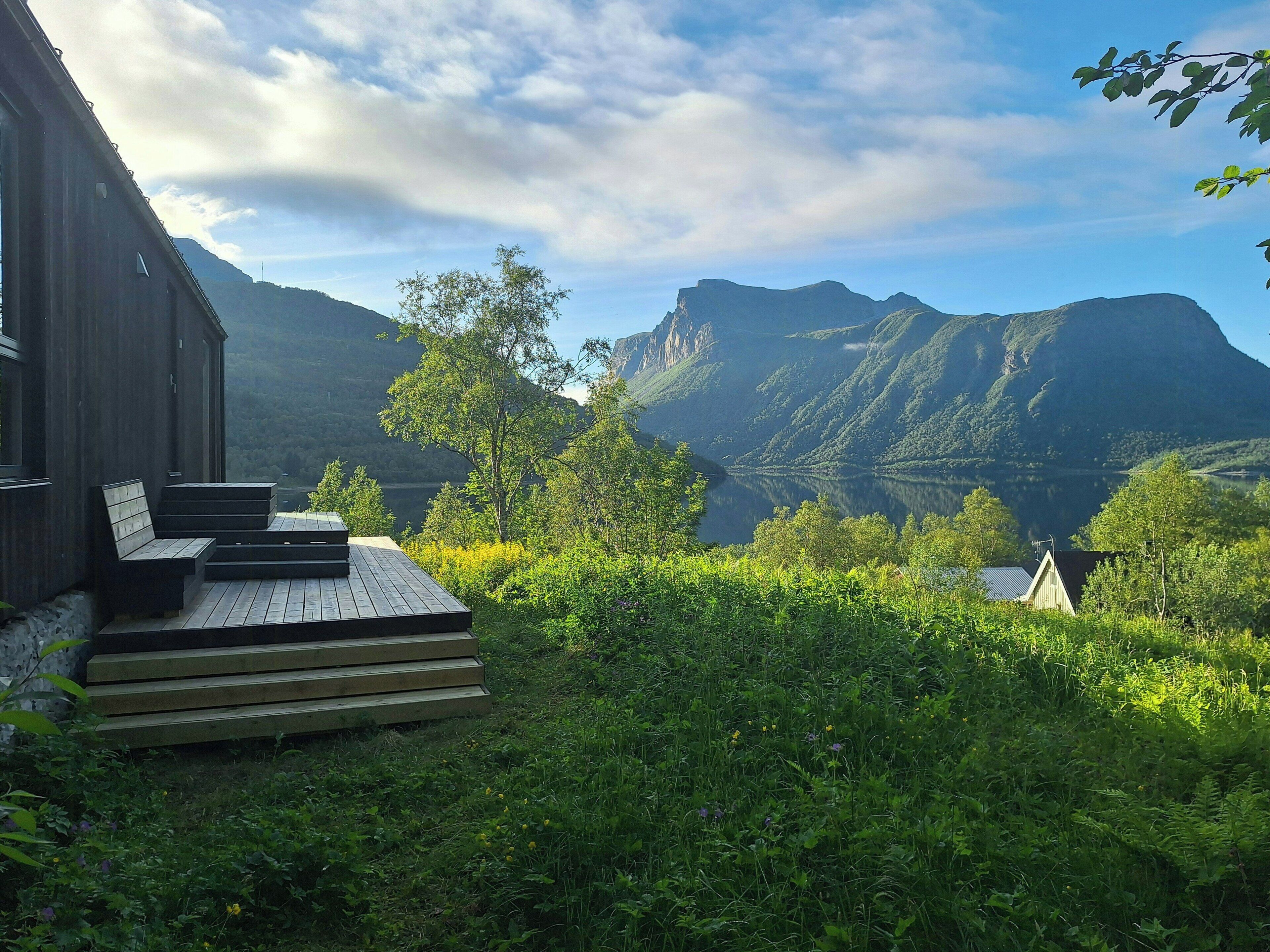 Ein Holzhaus mit einer Terrasse und Treppen zu einer Aussichtsplattform mit Blick auf Berge und einen See.