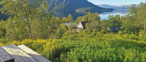 A wooden deck overlooking a mountainous landscape with a lake and houses in the background.