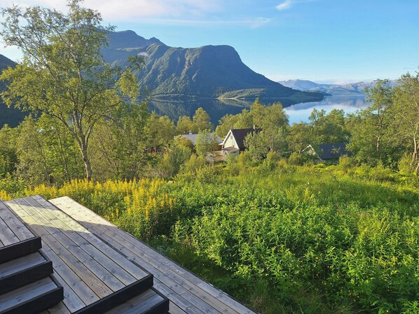 A wooden deck overlooking a mountainous landscape with a lake and houses in the background. - Cabin with sauna and fire pit (Nordland)