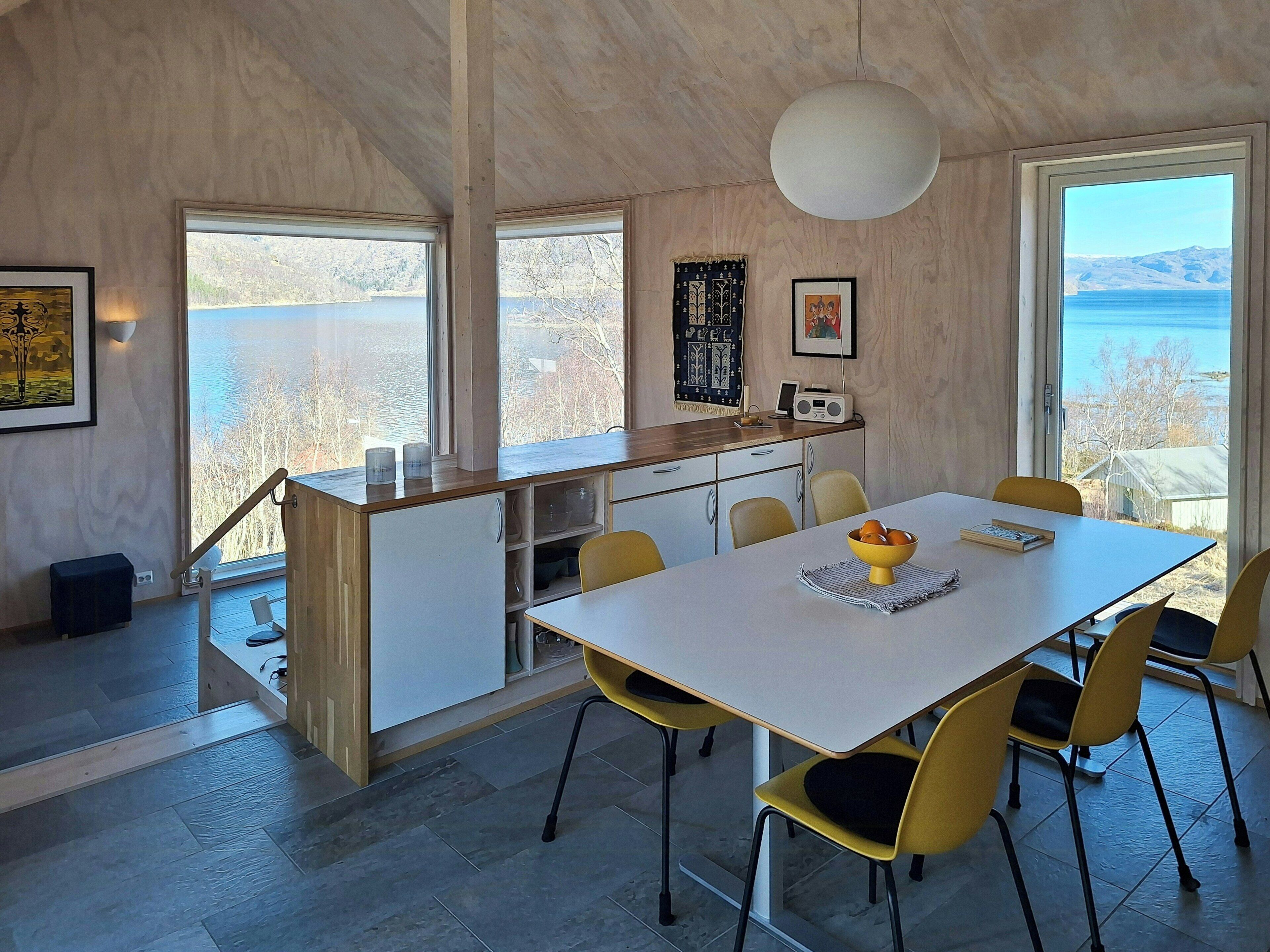 A modern kitchen with a dining area, large windows, and a view of the sea.