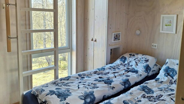 Makuuhuoneessa on kaksi sänkyä, puuseinät, ikkuna ja ovi.