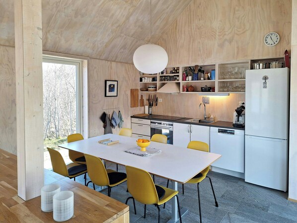 A modern kitchen with white cabinets, a white refrigerator, and a dining table with yellow chairs. - Cabin with sauna and fire pit (Nordland)