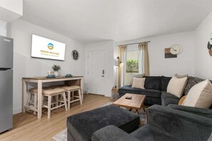 Ein modernes Wohnzimmer mit einer Couch, einem Esstisch mit Stühlen, einem kleinen Couchtisch und einem Kühlschrank.