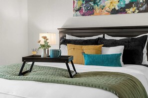 Ein ordentlich bezogenes Bett mit einer grünen Tagesdecke, ein Nachttisch mit einem Blumenstrauß und einer Lampe.