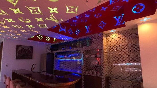 Una zona de bar con mostrador y taburetes, un área de estar con sofá y una pared decorada con un logotipo.