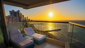 Un balcón con dos sillones de descanso y vista al océano al atardecer.
