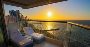 Ein Balkon mit zwei Loungestühlen und Blick auf das Meer bei Sonnenuntergang.