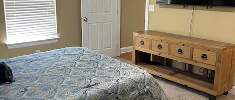 Ein Schlafzimmer mit einem Bett, einem Holzschrank, einem Deckenventilator, einer Tür und einem an der Wand befestigten Fernseher.