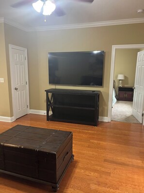 A room with a flat-screen TV mounted on the wall, a dark wooden entertainment center, and a large black trunk in the foreground.