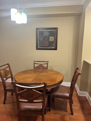 A dining area with a round wooden table and four chairs, a decorative wall piece, and a hanging light fixture.
