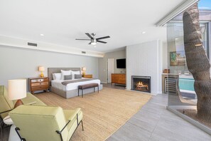 Een moderne slaapkamer met een bed, nachtkastjes, een televisie, een open haard en uitzicht op een zwembad.