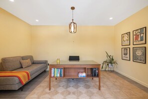 Ein Zimmer mit einer Couch, einem Tisch mit Bücherregal, einer Pendelleuchte und gerahmten Kunstwerken an der Wand.
