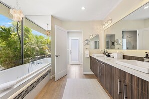 Een moderne badkamer met een bad, een grote spiegel en uitzicht op groen.