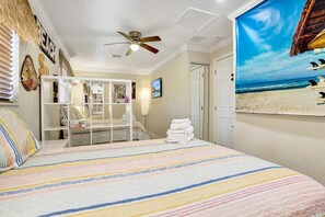A bedroom with a bed, a ceiling fan, a beach-themed wall mural, and a window with blinds. - Coral Reef Beach House (Lauderdale-by-the-Sea)