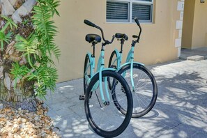 Two bicycles parked on a paved surface next to a building with a window and a door. - Coral Reef Beach House (Lauderdale-by-the-Sea)