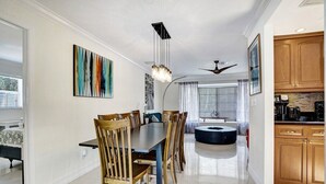 Un coin repas avec une table ronde et des chaises, un ventilateur de plafond et une cuisine dotée de meubles en bois.
