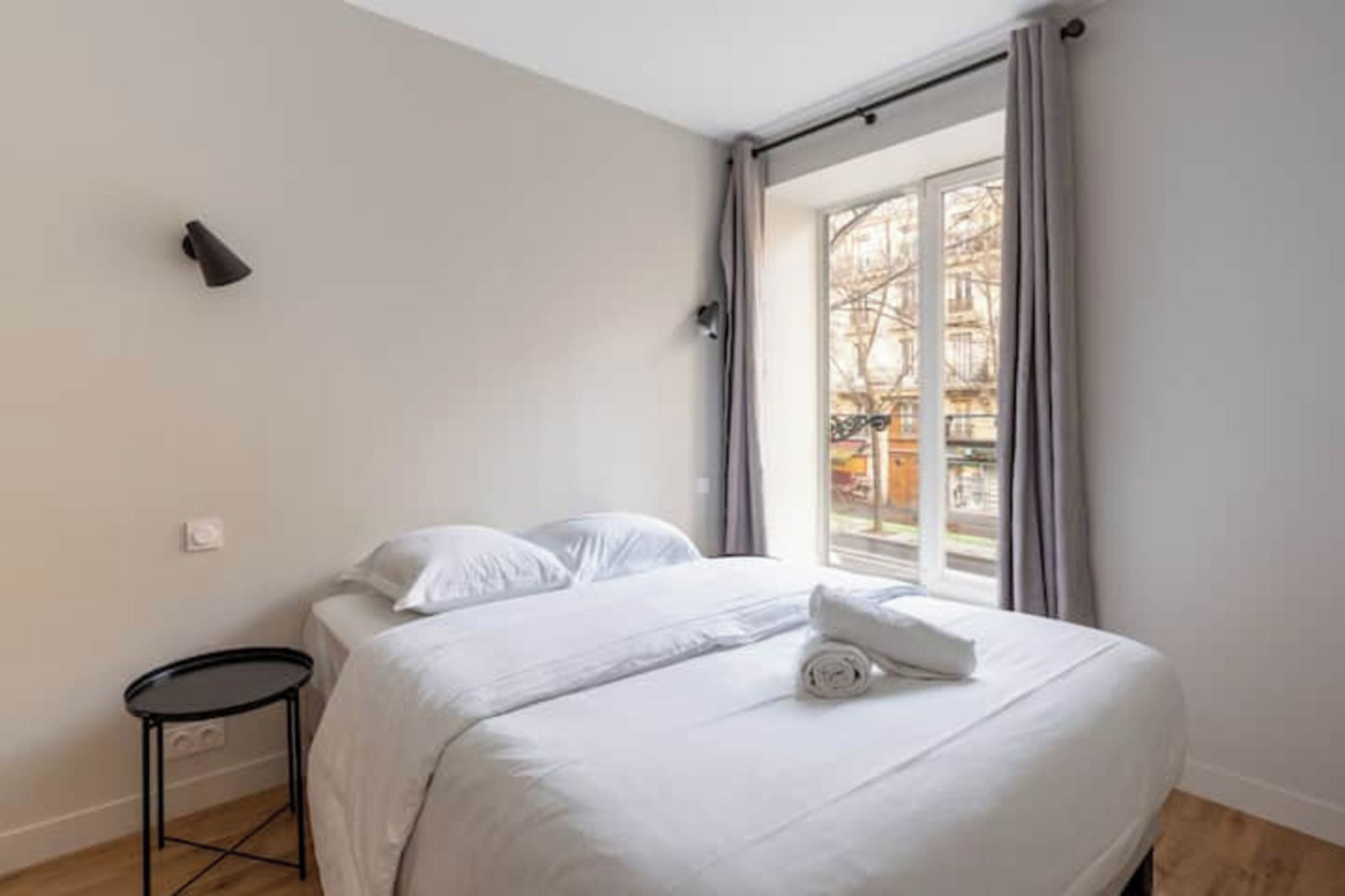 A bedroom with a bed, a small round table, and a window with curtains.