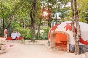 Un espace extérieur doté d’un four en briques, entouré d’arbres et de verdure.