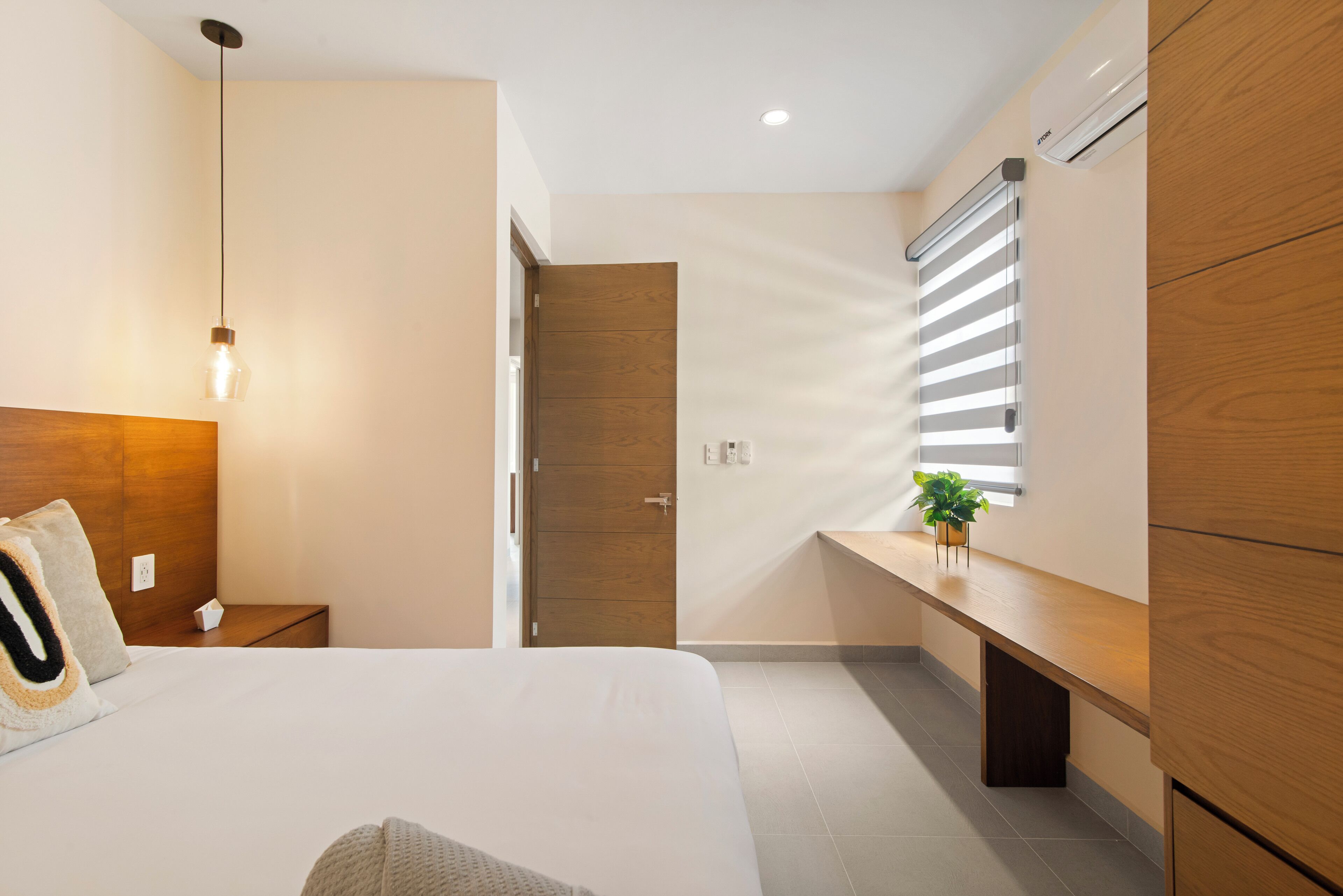 Ein modernes Schlafzimmer mit Bett, Nachttisch, Lampe, Kleiderschrank und einem Fenster mit Jalousien.