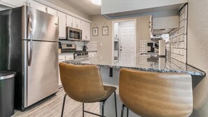 A kitchen with a stainless steel refrigerator, a microwave, and a stove. There are two bar stools and a granite countertop. - Newly Remodeled 3 BR House w/ Fire Pit, 5 min. From Stadium! (Norman)