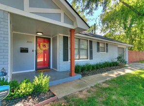 A single-story house with a red door, a mailbox, and a number '2020' on the door. - Newly Remodeled 3 BR House w/ Fire Pit, 5 min. From Stadium! (Norman)
